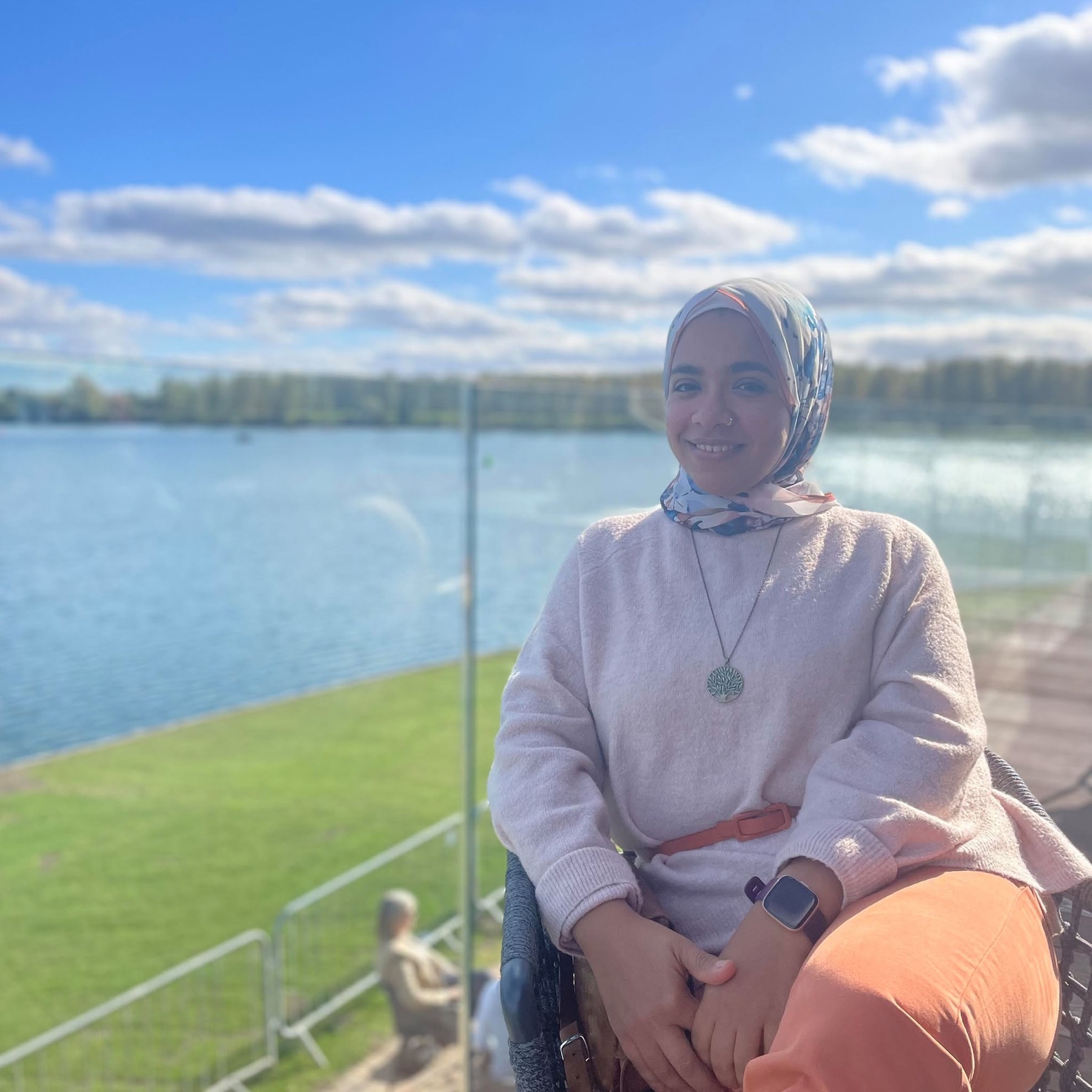 Amira Qassim smiling, seated by a lake on a sunny day